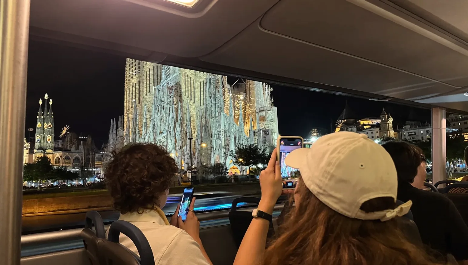 Turistas en un autobús descubierto contemplando los monumentos iluminados de Barcelona de noche